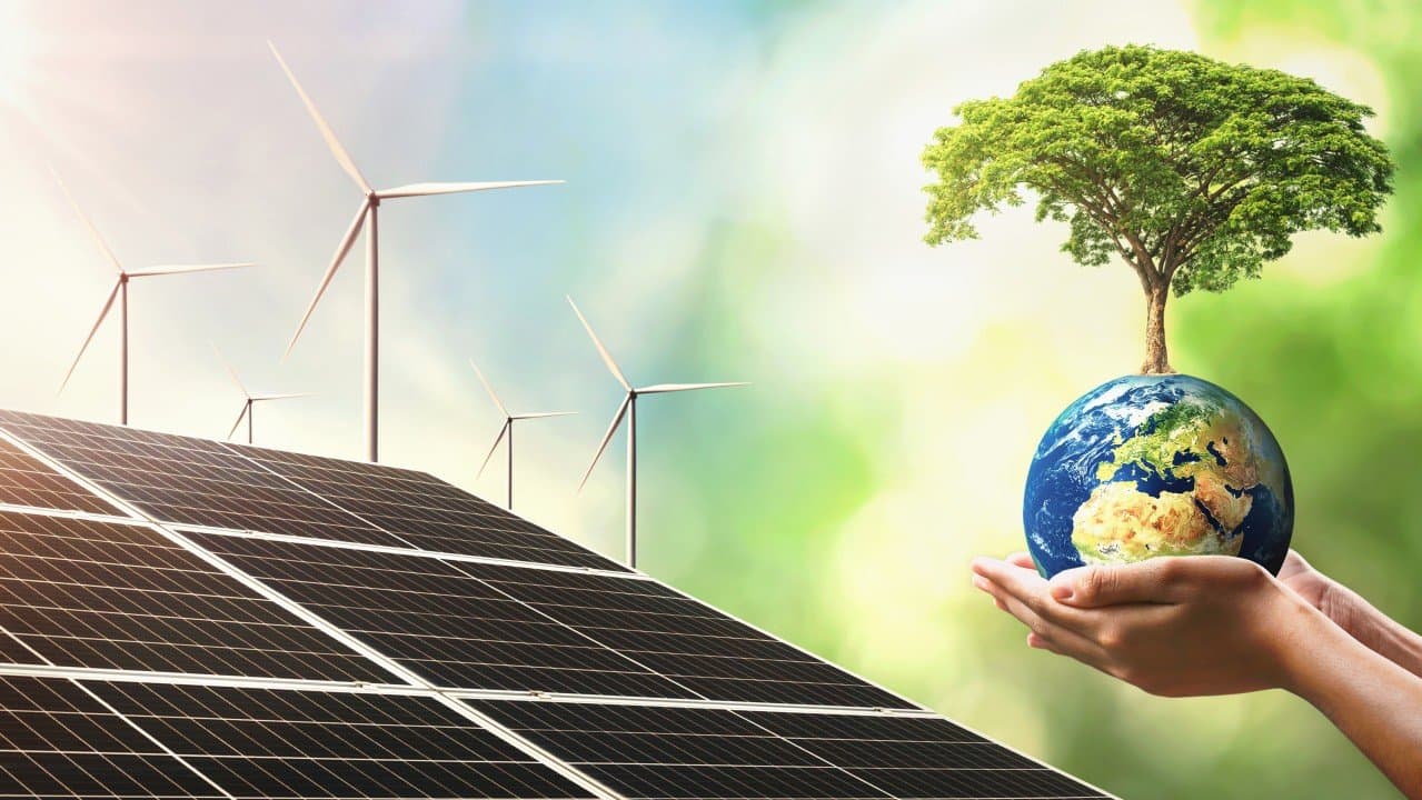 Panneaux solaires et éoliennes, et un arbre poussant sur un globe tenu dans des mains